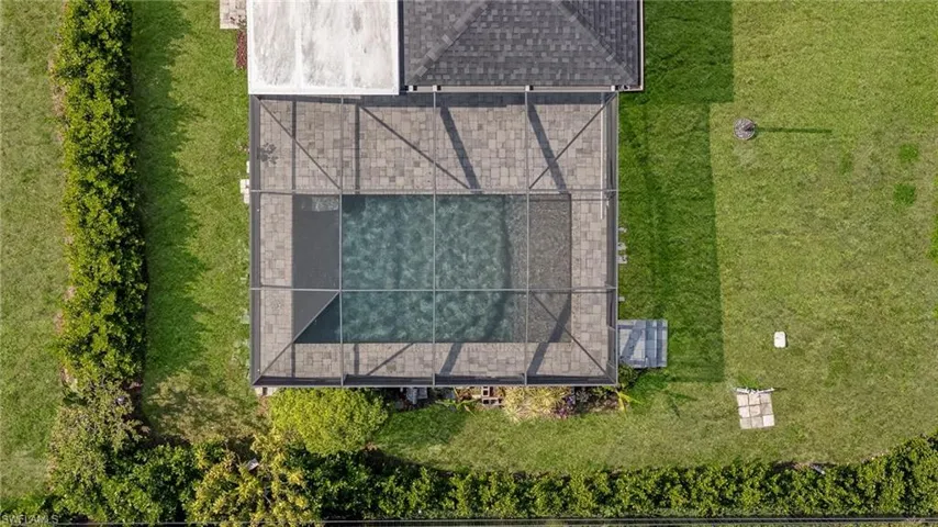 Screened swimming pool enclosure with paver decking, surrounded by a manicured lawn and mature privacy hedges