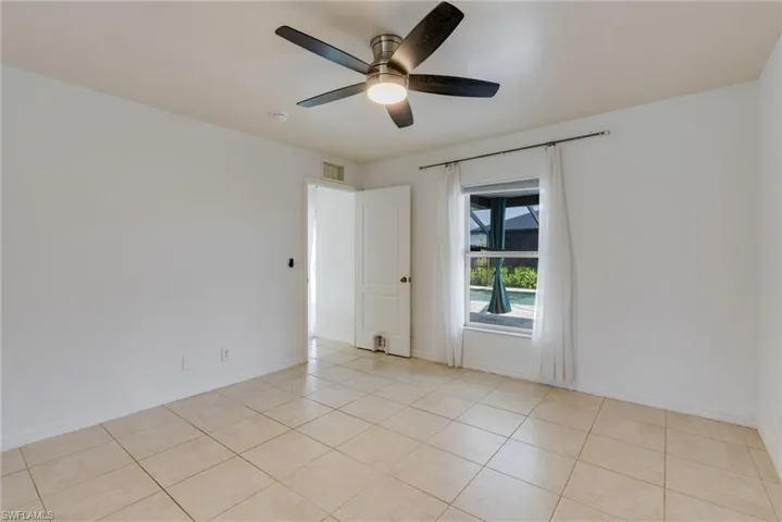 Room featuring neutral tile flooring, white walls, a ceiling fan with integrated lighting, and a window overlooking a screened pool area