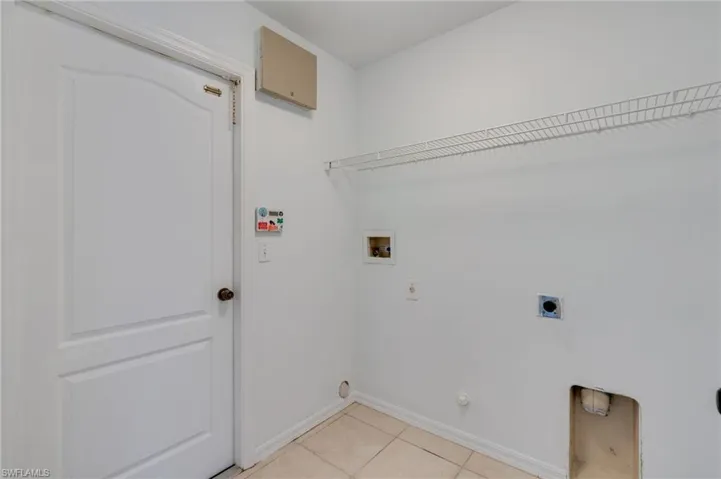 Utility area with ceramic tile flooring, a paneled door, wall-mounted wire shelving, and appliance hookups