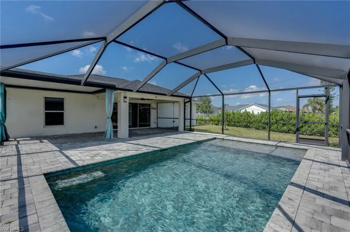 Screen-enclosed pool area featuring a rectangular pool with integrated steps, surrounded by a paver patio