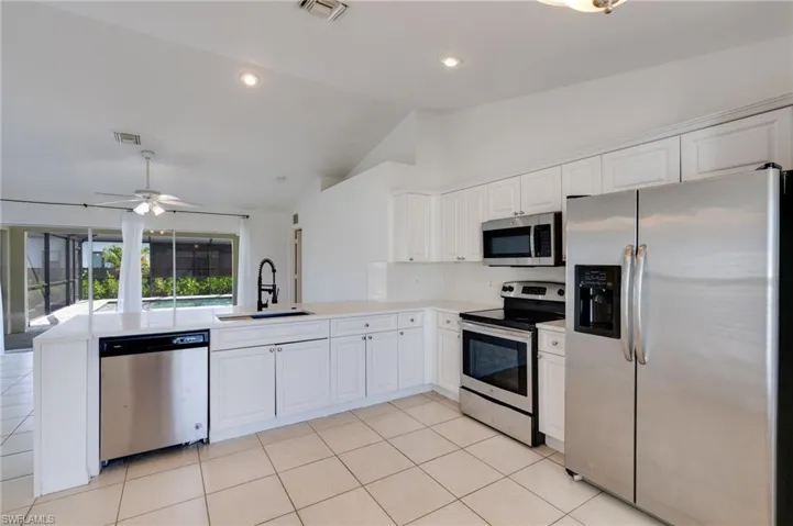 White kitchen cabinetry with stainless steel appliances, a white tile backsplash, and light-toned countertops