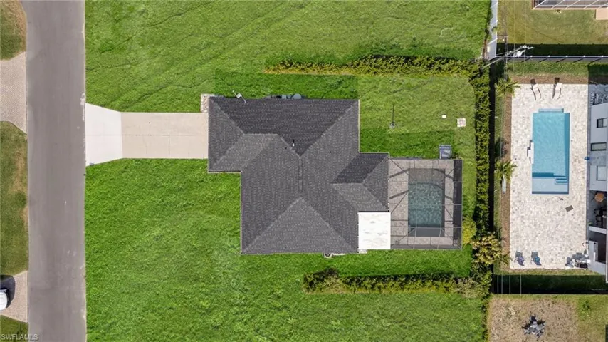 Single-story residence featuring a dark shingle roof, a screened-in pool enclosure, and an expansive concrete driveway