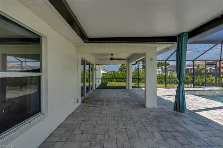 Spacious screened lanai featuring extensive paver flooring, overhead ceiling fan, and direct access to the pool area