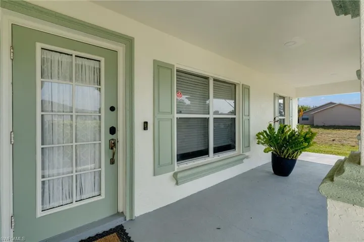 Covered entry featuring a transom window above the front door, glass-paneled front door, window shutters, and stucco exterior finish