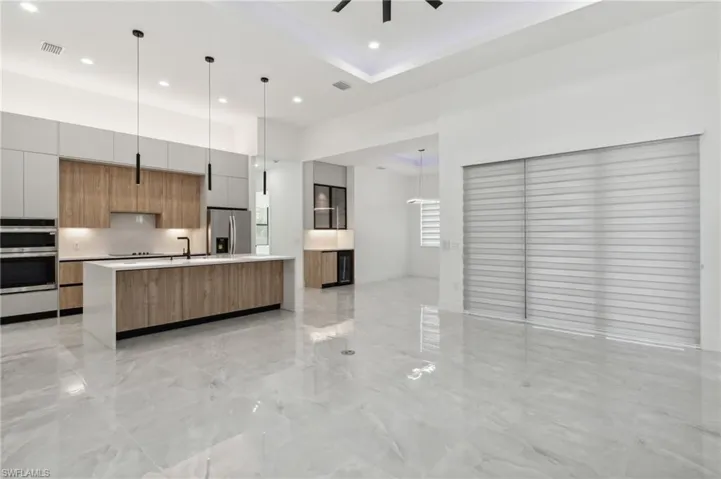 Kitchen featuring a large island with sink, sink, ceiling fan, stainless steel appliances, and decorative light fixtures