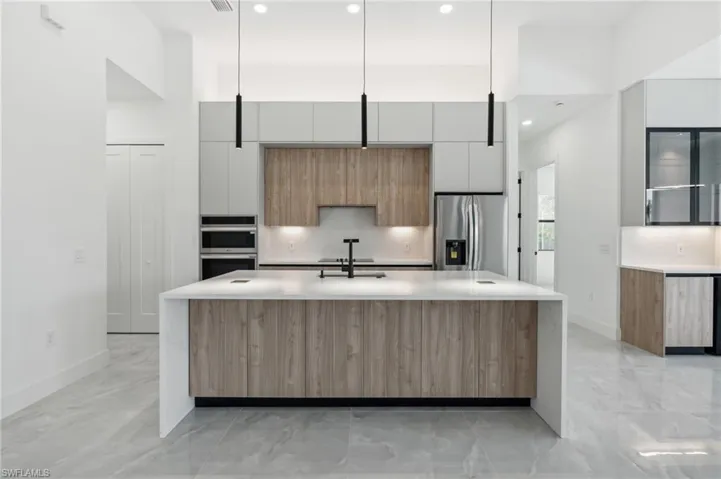 Kitchen with sink, white cabinetry, stainless steel appliances, decorative light fixtures, and a kitchen island with sink