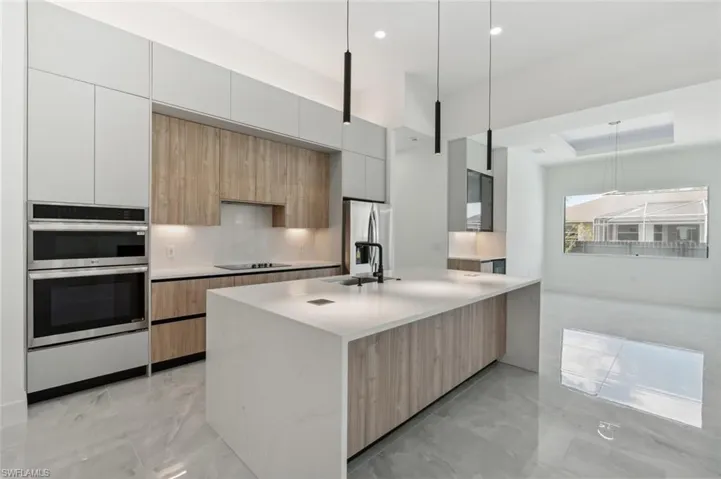 Kitchen with a center island with sink, sink, pendant lighting, white cabinetry, and appliances with stainless steel finishes
