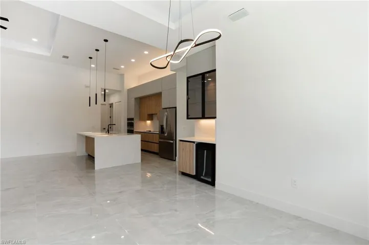Kitchen with gray cabinetry, a raised ceiling, stainless steel fridge, decorative light fixtures, and a center island with sink