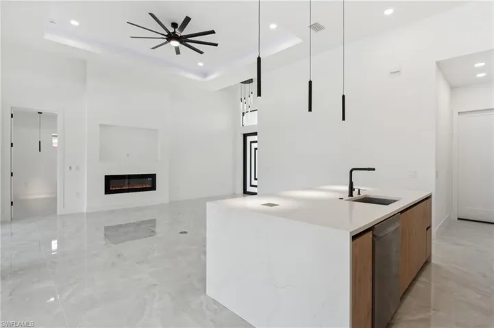 Kitchen with a center island with sink, hanging light fixtures, a raised ceiling, stainless steel dishwasher, and sink