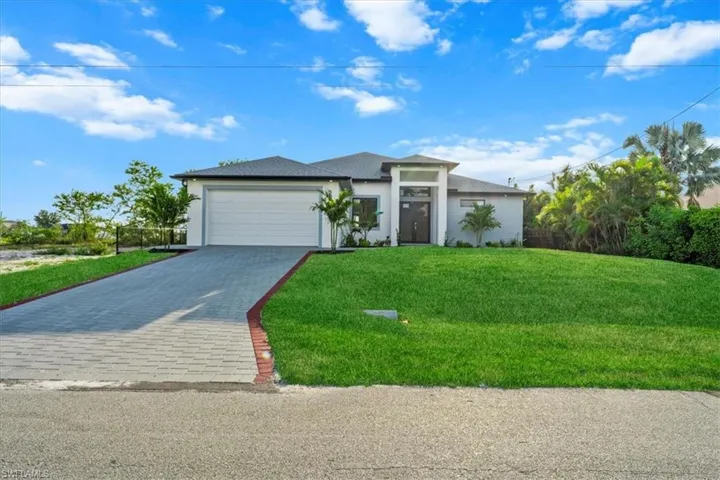 Prairie-style home with an attached garage, stucco siding, decorative driveway, and a front yard