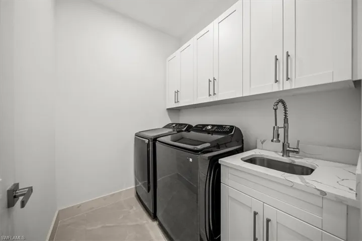 Laundry area featuring washing machine and clothes dryer, cabinet space, baseboards, and light marble finish floors