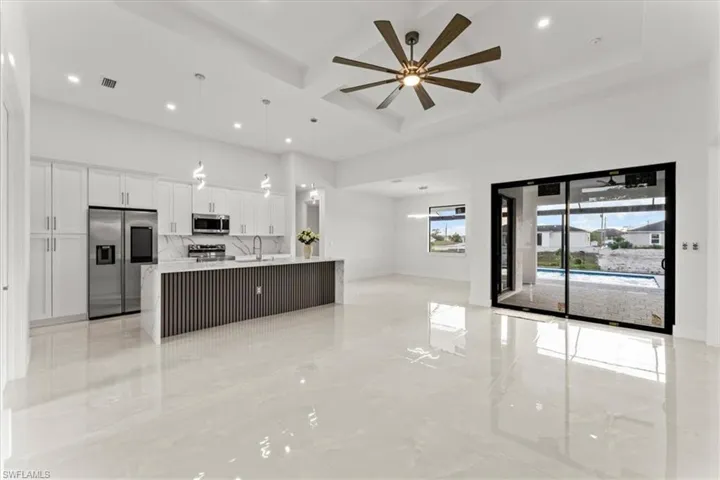 Kitchen with stainless steel appliances, open floor plan, a sink, coffered ceiling, and white cabinetry