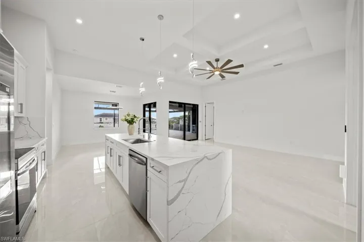 Kitchen featuring a sink, stainless steel appliances, coffered ceiling, white cabinetry, and a large island