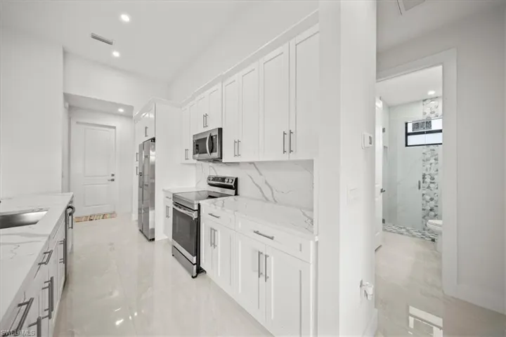 Kitchen with appliances with stainless steel finishes, light stone counters, white cabinets, recessed lighting, and decorative backsplash