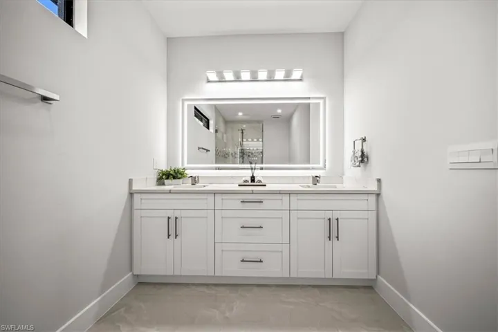 Full bathroom with baseboards, marble look tiles, double vanity, and a shower