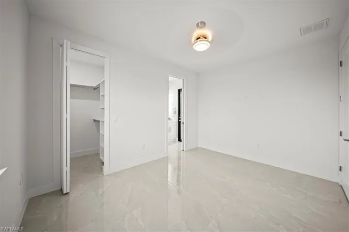 Unfurnished bedroom with light marble finish flooring, a spacious closet, baseboards, and a closet