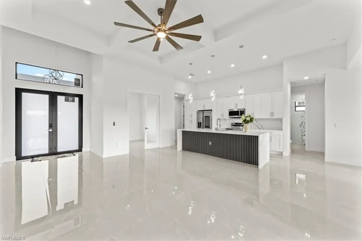 Unfurnished living room with a towering ceiling, coffered ceiling, recessed lighting, a sink, and french doors