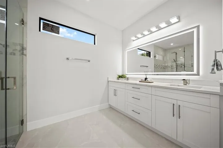 Bathroom featuring marble tiled flooring, double vanity, a marble finish shower, and baseboards