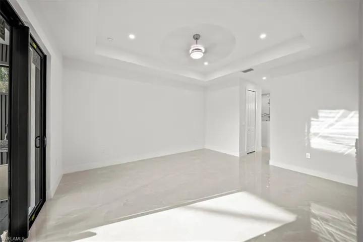 Empty room featuring a raised ceiling, a ceiling fan, recessed lighting, light marble finish flooring, and baseboards