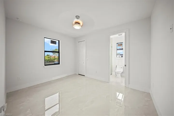 Unfurnished bedroom featuring light marble finish flooring, connected bathroom, baseboards, a closet, and a ceiling fan