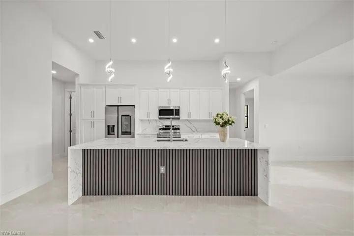 Kitchen featuring appliances with stainless steel finishes, white cabinets, a spacious island, light stone countertops, and recessed lighting