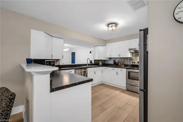 Kitchen featuring white cabinetry, stainless steel appliances, backsplash, light wood plank porcelain tile flooring
