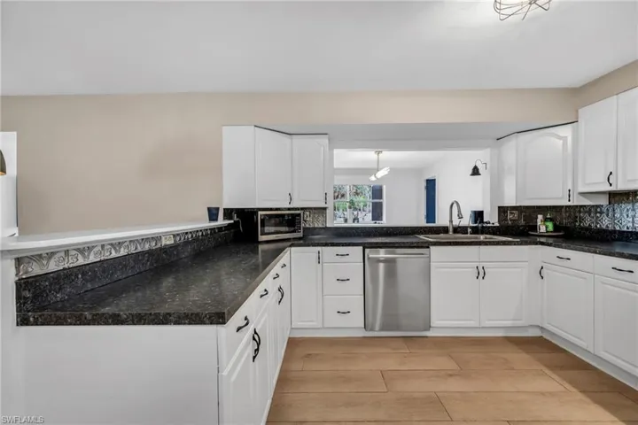 Kitchen featuring white cabinetry, stainless steel appliances, backsplash, light wood plank porcelain tile flooring