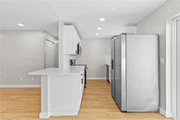 Kitchen with appliances with stainless steel finishes, white cabinetry, a peninsula, light wood-style flooring, and recessed lighting