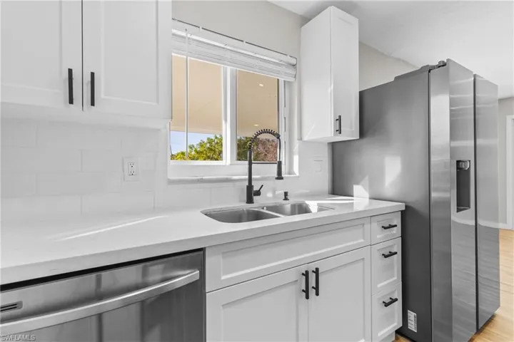 Kitchen featuring white cabinets, stainless steel appliances, decorative backsplash, light wood-type flooring, and light stone countertops