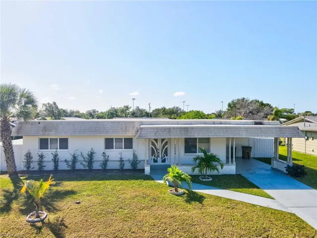 View of front facade with a front yard, stucco siding, driveway, covered porch, and an attached carport
