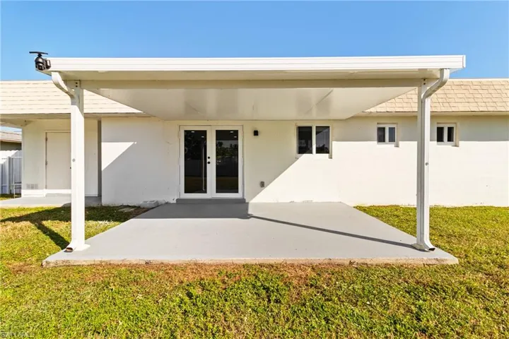 Rear view of property featuring a patio, a lawn, stucco siding, and french doors