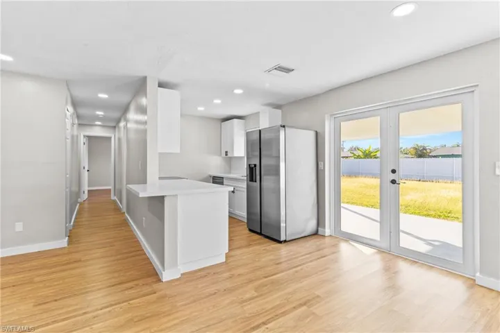 Kitchen featuring white cabinetry, stainless steel refrigerator with ice dispenser, a peninsula, french doors, and light wood-type flooring