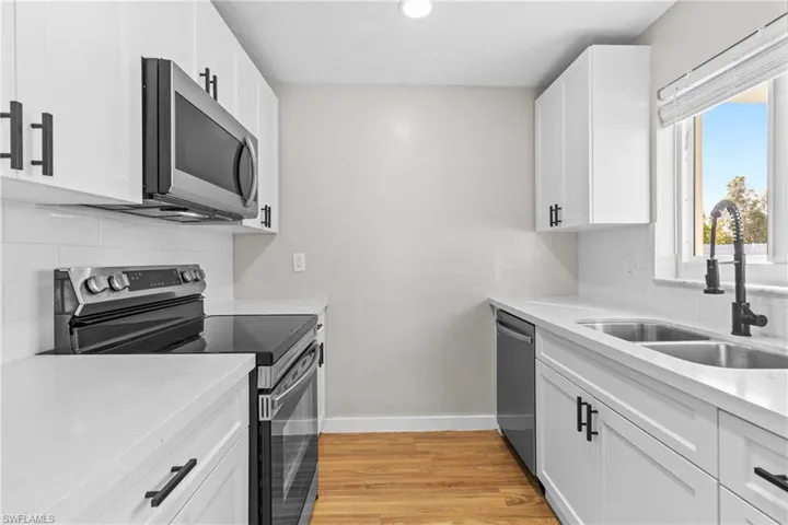 Kitchen with decorative backsplash, stainless steel appliances, white cabinetry, light wood finished floors, and light stone counters