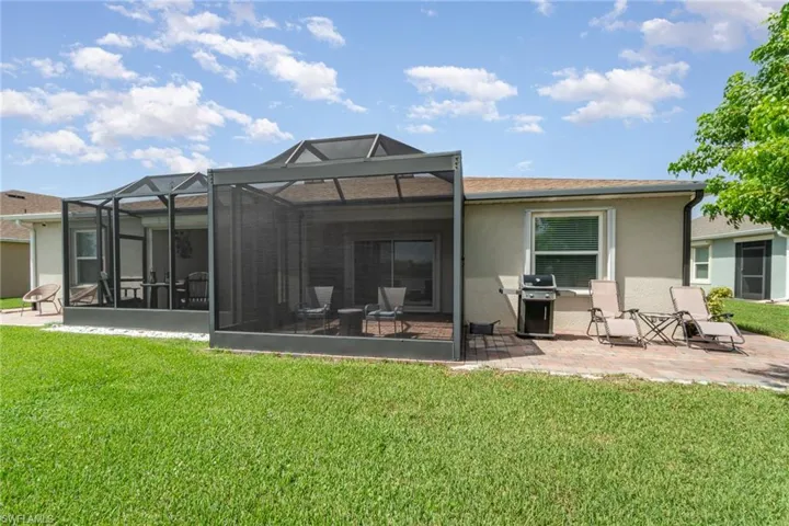Rear view of property featuring screened enclosure, a lawn, and a patio