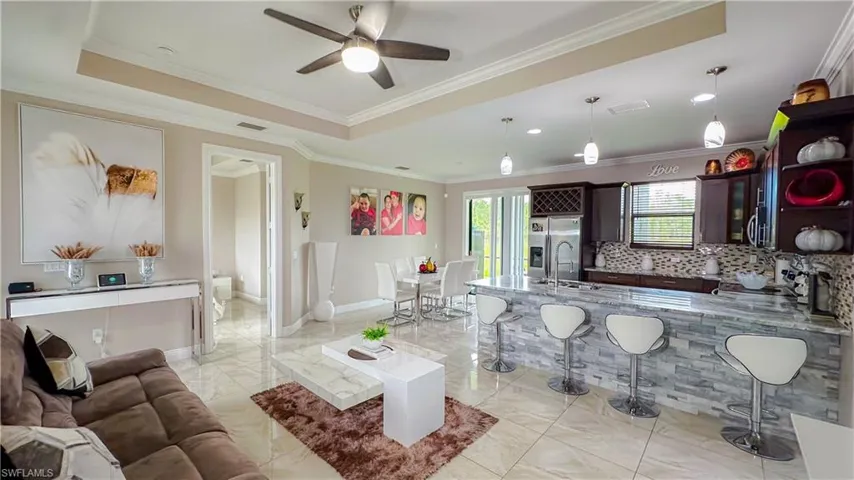 Tiled living room with ceiling fan, sink, a tray ceiling, and ornamental molding