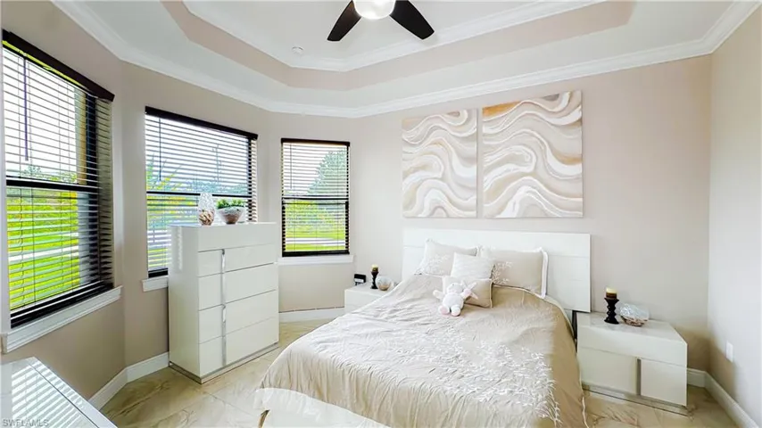 Tiled bedroom with ornamental molding, ceiling fan, and a raised ceiling