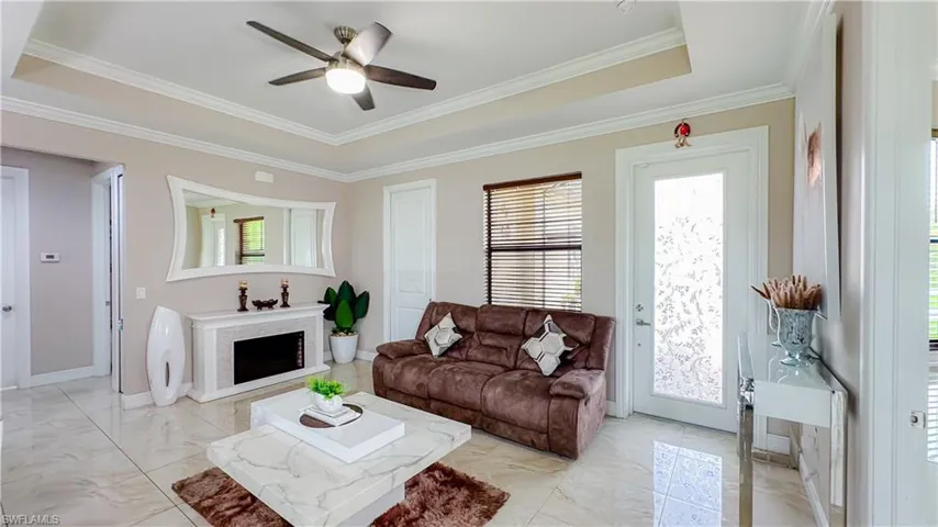 Tiled living room with ceiling fan, a tray ceiling, and ornamental molding