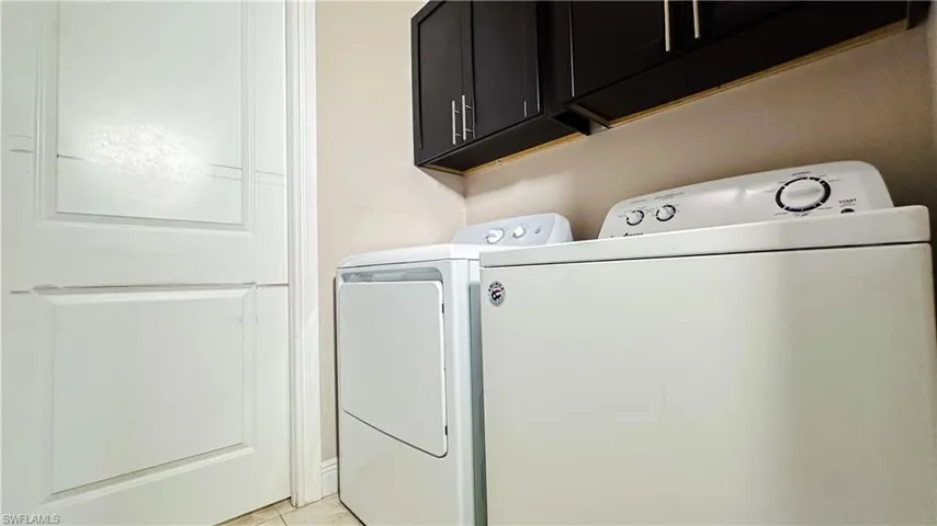 Clothes washing area featuring light tile patterned floors, separate washer and dryer, and cabinets