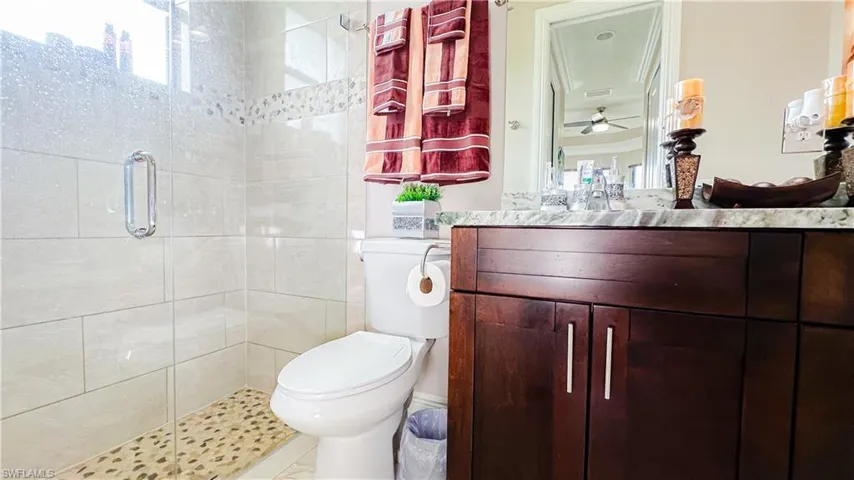 Bathroom with vanity, ceiling fan, a shower with shower door, toilet, and tile patterned flooring