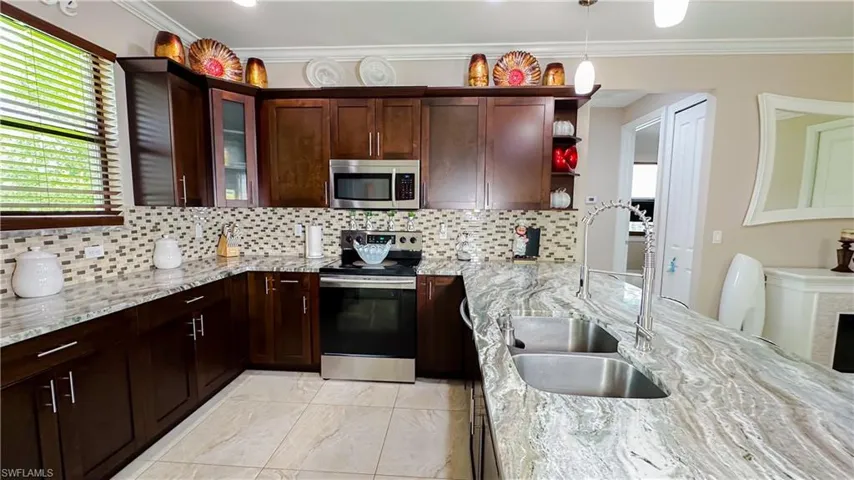 Kitchen with appliances with stainless steel finishes, tasteful backsplash, light stone counters, and light tile patterned floors