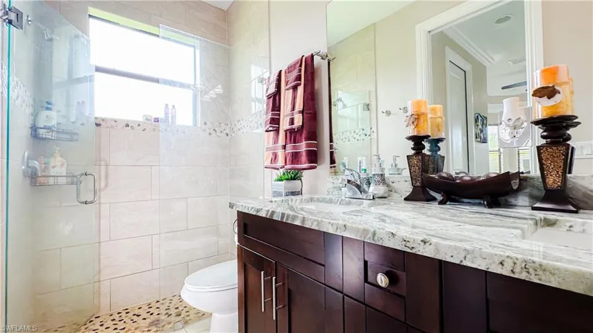 Bathroom featuring crown molding, a shower with shower door, toilet, vanity, and tile walls