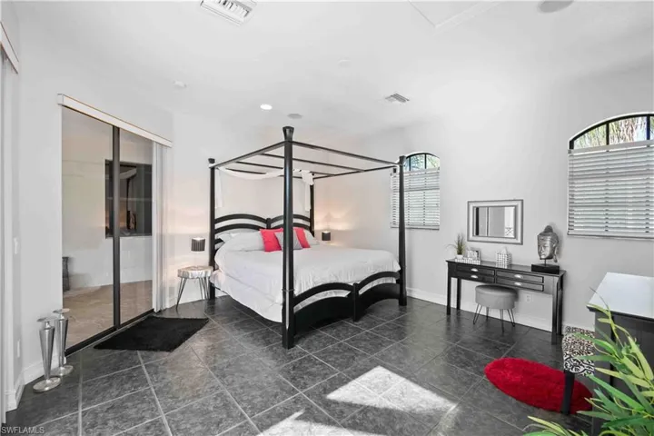 Spacious room featuring dark tile flooring, arched windows with blinds, a built-in recessed ceiling light, and a sliding glass door