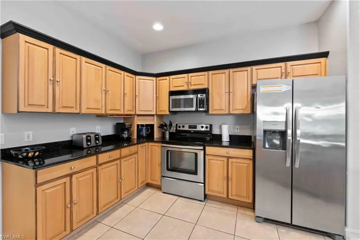 Spacious kitchen featuring light wood cabinetry with black crown molding, dark countertops, stainless steel appliances, and tiled flooring
