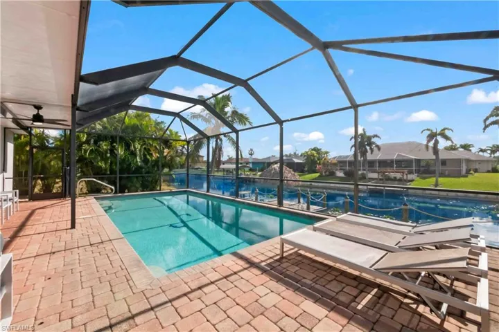 Screened-in pool area featuring a rectangular swimming pool, brick paver decking, and direct water access