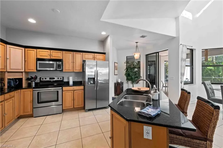Kitchen featuring a center island with sink, stainless steel appliances, decorative light fixtures, dark stone countertops, and sink