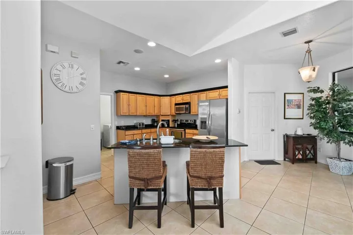 Open-concept kitchen featuring wood cabinetry, black countertops, and stainless steel appliances