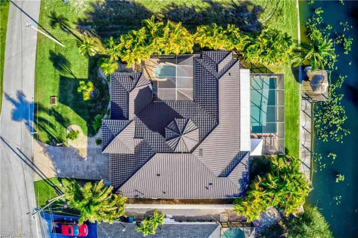 Overhead view of a property featuring a metal roof, screened pool enclosure, additional screened patio, and waterfront access with a boat dock