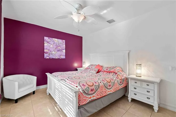 Bedroom featuring a purple accent wall, white ceiling fan with integrated lighting, and tile flooring