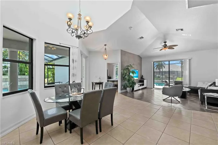 Dining space with ceiling fan with notable chandelier, light tile patterned floors, and vaulted ceiling