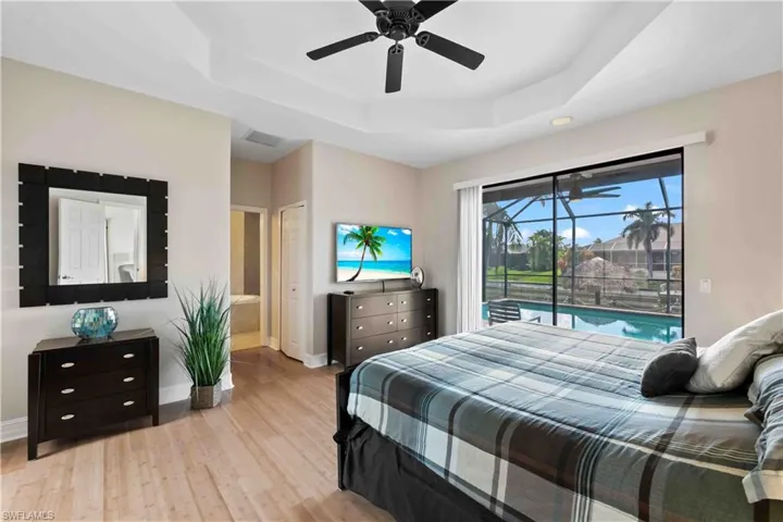 Master bedroom featuring wood-finish flooring, a tray ceiling, and a ceiling fan